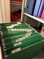 Green hanging file folders arranged in a filing cabinet with alphabetic tab labels A through Y, missing Q, X, Z tabs.
