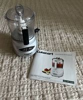 Front view of the Cuisinart Mini-Prep Plus food processor with instruction booklet beside it, showing the clear plastic bowl, black handle, and silver base with two control buttons.