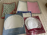 Various paper doilies including white, pink, and blue rectangular and round styles, some still in packaging.