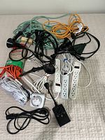 Photo shows multiple extension cords in various colors and lengths along with power strips, electrical timers, and adapters.