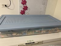 Side view of Rubbermaid storage bin lid and partially visible contents including colorful wrapping paper and gift bags