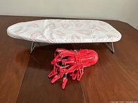 Image of smaller ironing board with removable cover showing top surface and red patterned fabric.