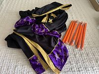 Photo showing the vintage Halloween cloak in black fabric with gold trim and purple velvet cuffs adorned with stars and embellishments, along with all seven orange taper candles grouped beside it.