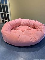 Front view of the soft, velvety pink donut-shaped pet bed with padded sides and tufted base cushion.