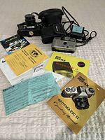 Main assortment of cameras and associated documentation and accessories laid out on white fabric.