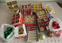 A large collection of vintage Christmas ornaments grouped in a pile showing boxes and loose ornaments with gold, red, and green colors.