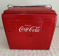 Front view showing Coca-Cola white logo on red metal cooler with visible wear and scratches.