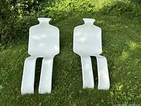 Two white fiberglass figure lounge chairs placed side by side on grass, showing full shapes and proportions