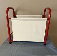 Front view of vintage IKEA magazine rack showing red metal frame and white plasticized canvas holder.
