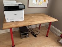 Rectangular wood topped table with a Canon printer on it, showing the table surface, legs, and floor context.