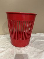 Red plastic vintage IKEA wastebasket standing upright, showing cylindrical shape, vertical slats, and smooth top rim.