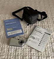Sony Cyber-shot DSC-P72 digital camera with manuals and black carrying case on white textured surface.