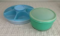 Blue Tupperware round party platter with five compartments next to green Tupperware round bowl with lid on a textured light surface.