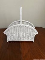 Front view of vintage white wicker magazine basket showing woven pattern and curved handle.