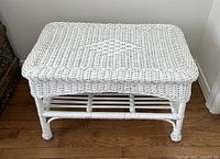 Front view of the vintage white wicker side table showing woven top surface and lower storage shelf.