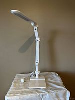 Full view of white adjustable desk lamp extending from rectangular base with power cord visible