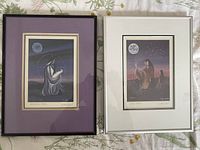Two framed prints "June's Moon" and "December's Moon" side by side on floral tablecloth. Both prints double matted with differing mat colors and black frames.