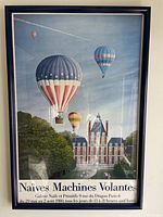 Full view of the framed vintage hot air balloon poster with multiple balloons floating above a French chateau surrounded by trees.
