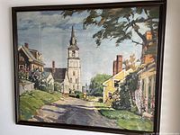 Full view of the framed painting showing the street, houses, church steeple, trees, and two figures.