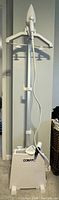 Full view of Conair garment steamer base unit with hose and handheld steamer attached on tall stand.