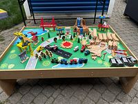 Full view of KidKraft train table with all included accessories arranged on surface. Shows trains, tracks, vehicles, figures, buildings, and play features.