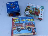 Three kids puzzles displayed: Melissa & Doug Giant Fire Truck floor puzzle, Ludattica Under the Sea puzzle with blue box and 3D glasses, and ShapeTown Crocodile Creek floor puzzle box with colorful town illustration and geometric shapes.