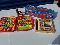 Photo of open alphabet puzzle with colorful uppercase letters in two red carrying case halves, Melissa & Doug animal stamp set with four colored markers, and beginner's balance scale boxed set.