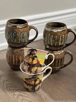 Four vintage McIntosh heavy ceramic mugs stacked in pairs with two contemporary Group of Seven mugs in front.