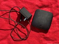 Black Xiaomi Mi Box Android TV device with matte finish and 'mi' logo on top, accompanied by a black power adapter with attached cable.