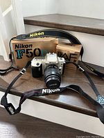Nikon F50D camera body with Zoom-Nikkor lens mounted and Nikon branded strap, along with camera and lens boxes on wooden surface.