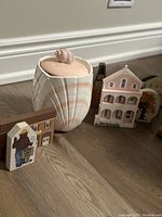 Pink seashell canister with lid and several hand-painted wood houses clustered around it on a wooden floor.