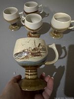 Five vintage ceramic pedestal mugs by Otagiri Japan. One mug is decorated with a brown harbor drawing while others are plain with brown and cream glaze.