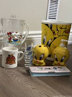 Overview photo of all items together including Tweety Bird bathroom items, Smurf shot glasses, Woodstock mug, Mickey and Minnie juice pitcher, and Minnie pencil case