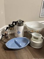 Lot of vintage kitchenware including Corningware coffeepot with Cornflower pattern, glass coffee carafes, Arabia Finland white casserole, blue Pyrex divided server, and smaller dishes.
