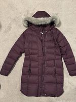 Front view of a women's burgundy Columbia down winter jacket with faux fur hood, showing full length and zipped pockets