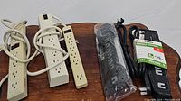 Five power strips/surge protectors arranged on wooden surface including three tan power strips and two black surge protectors including one CyberPower brand with label