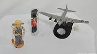 Three items on display: B-17 Flying Fortress statue, folk art corn husk doll, and British royal guard doll in plastic case.