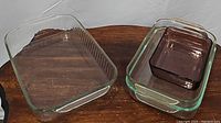 Four glass baking and casserole dishes on wooden surface showing one large ribbed clear glass dish and three other dishes nested, including a small purple Pyrex dish.