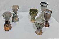 Full set of six pottery pedestal goblets arranged on a white background, showing color and style variety