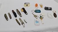 All items spread on a white surface showing the variety of pocket knives, key chains, and lighter