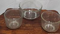 Three clear glass mixing bowls of different sizes arranged on a wooden surface, showing overall condition and size comparison.