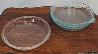 Photo showing one smooth-edged clear glass Pyrex pie plate and one blue-tinted fluted edge Pyrex pie plate with handles