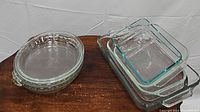 Four round clear glass pie plates (2 with fluted edges, 2 without) stacked and three rectangular Pyrex glass baking dishes nested, showing overall condition and style.