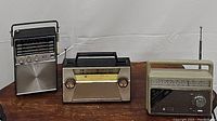 Three vintage transistor radios placed side by side on wooden table. From left to right: Arvin marine band radio, Fuji Denki two-band radio, General Electric 2-way power radio.