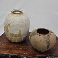Two ceramic vases on a wooden surface. Left: tall tan and cream vase with mustard mountain abstract design. Right: round vase with etched wing patterns.