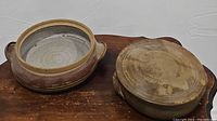 Top down and angle view of two stoneware pottery items on a wooden tray, showing interior and exterior of bowl and bottom of lidded dish.