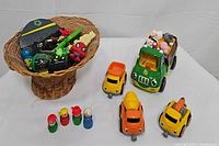 Basket with assorted toys including plastic figures and toy cars; wooden Fisher-Price people in front