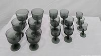 Photo showing 6 vintage smoke gray wine glasses, 6 sherry glasses, and 3 shot glasses arranged in rows on a white surface.