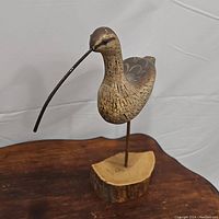 Brown bird carving with long curved beak mounted on natural wood base stand.