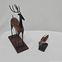 Large carved deer figurine and small painted woodpecker statue together on table.